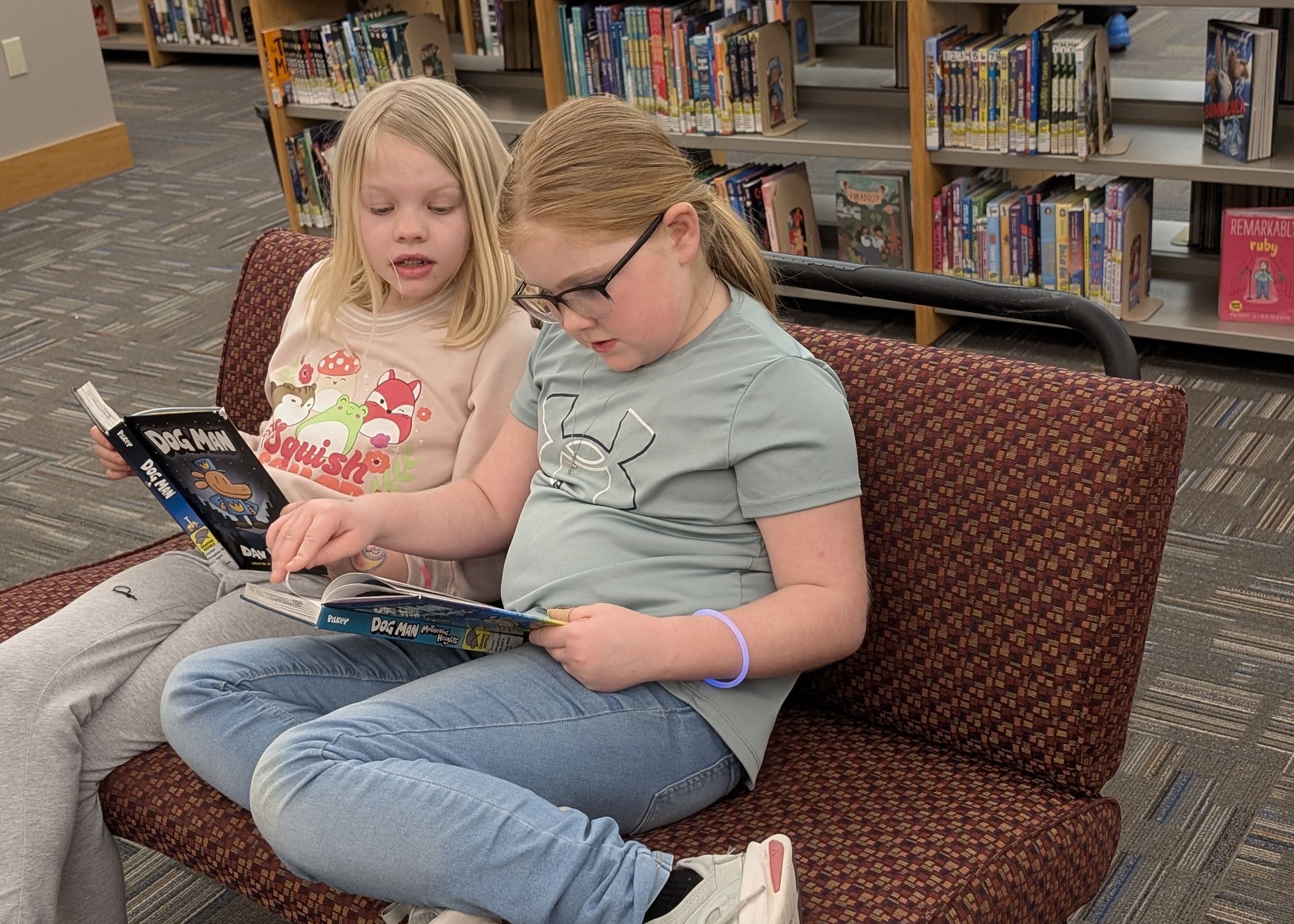 Two young girls curl up reading graphic novels